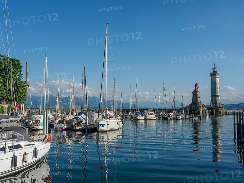 Boats in the harbour with a lighthouse and a lion statue in the background under a blue sky, Lindau, Bavaria, Germany, Europe