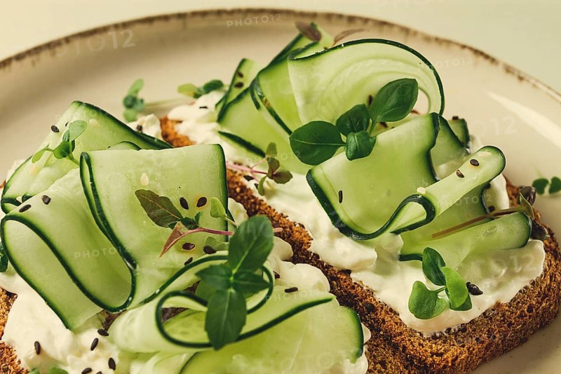 Breakfast, cereal bread sandwiches, cream cheese, sliced cucumber, with micro greenery on a light table, close-up, top view, selective focus, no people