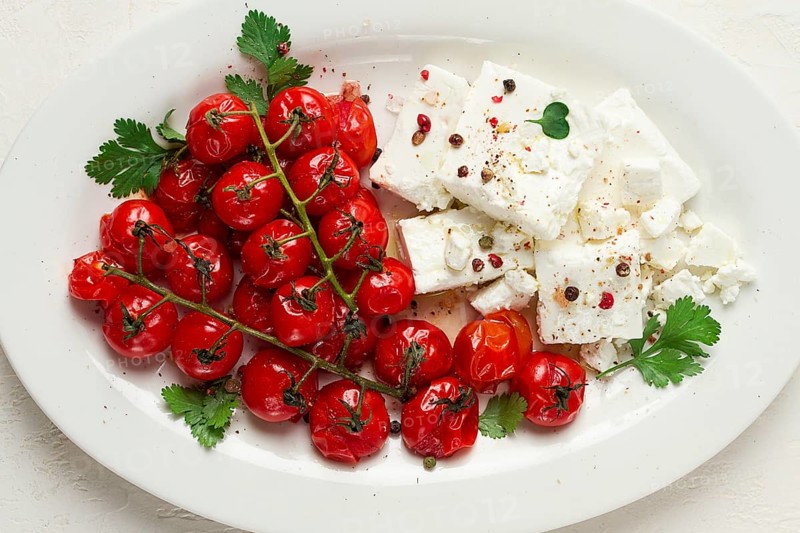 Gebackene Kirschtomaten, mit Käse und Gewürzen, auf einem weissen Teller, hausgemacht, keine Leute