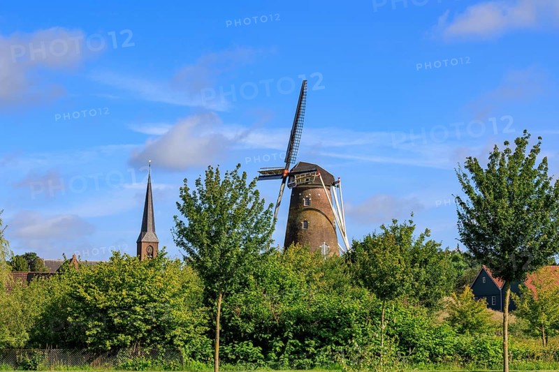 Landscape with windmill and church tower, surrounded by green trees and blue sky, bredevoort, gelderland, the netherlands