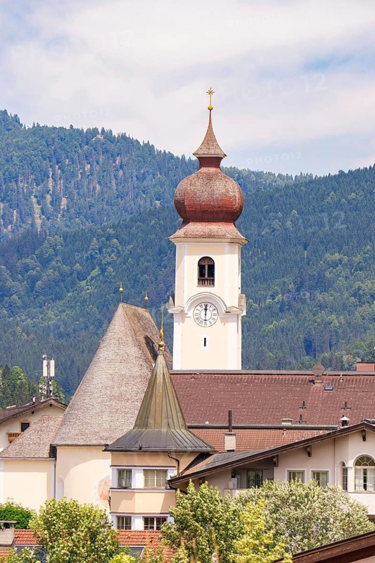 Church with high bell tower in a traditional alpine village, surrounded by mountains and many houses, Achernsee, Austria, Germany, Europe