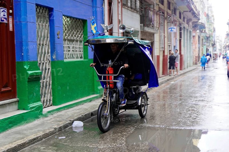 Havana, Cuba, Central America, man riding a cycle rickshaw on a wet road in an urban environment, Central America