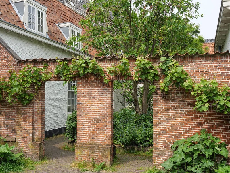 Idyllic garden with green brick arch and surrounding old buildings, Leiden, Netherlands