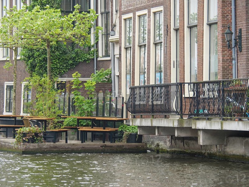Urban canal with neighbouring buildings and metal balcony balustrades, next to tables and chairs by the water, Leiden, Netherlands