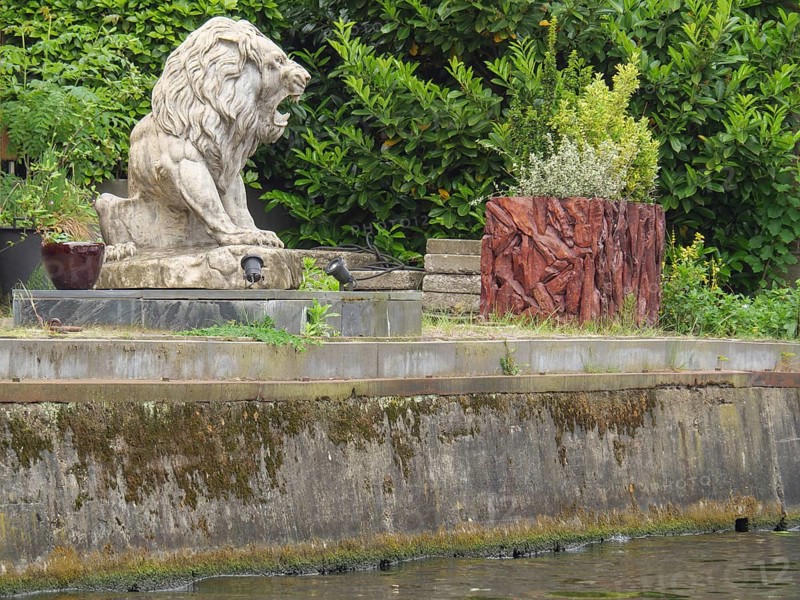 Stone statue of a lion on an overgrown and watered stone bank surrounded by nature, Leiden, Netherlands