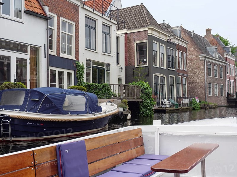 A boat moored in front of a row of townhouses on the canal on a calm, cloudy day, windows with curtains, Leiden, Netherlands