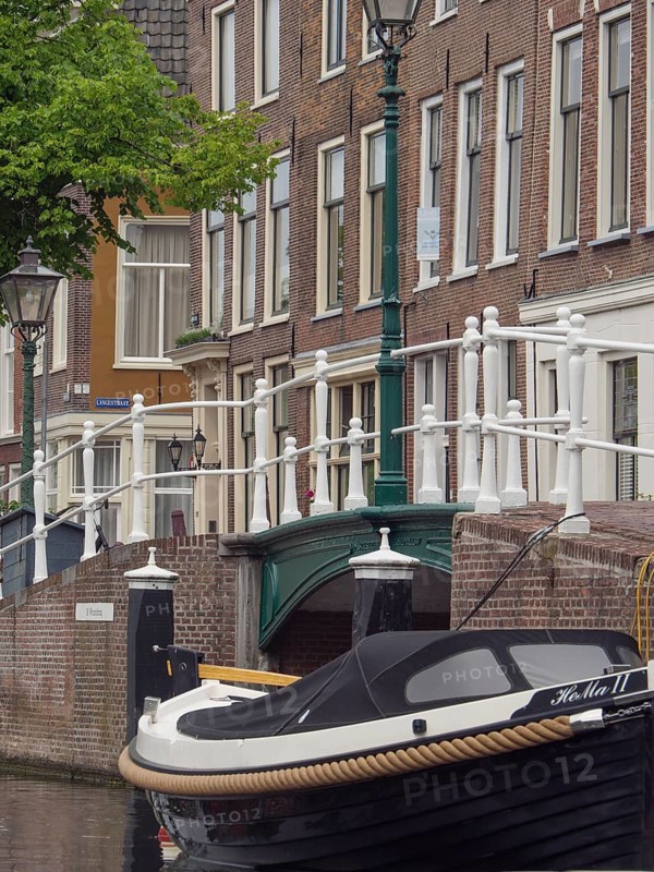 An elegant boat moored by a bridge, surrounded by historic city buildings and lanterns on a canal, Leiden, Netherlands