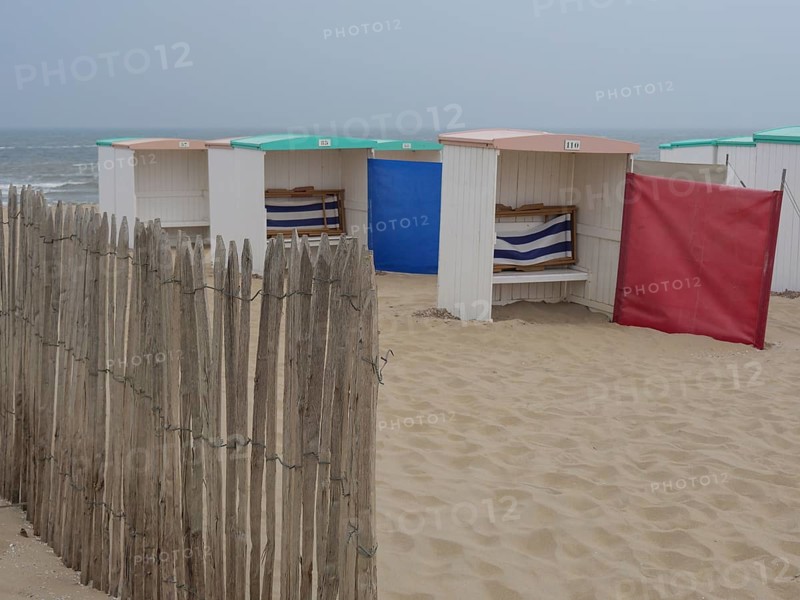 Beach huts on a sandy beach with wooden fence and sun protection in front of the ocean, Leiden, Netherlands