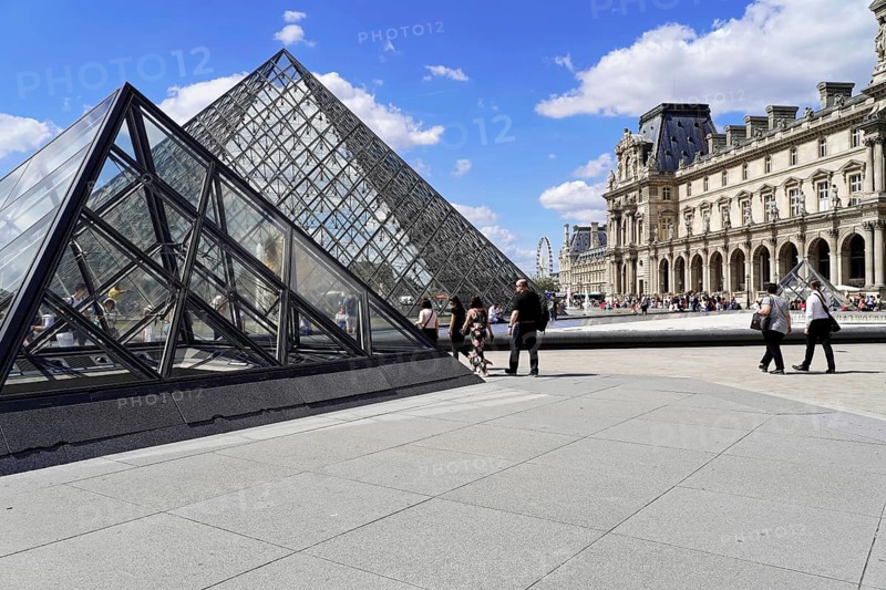 Glass pyramid in the courtyard of the Palais du Louvre, Paris, France, Europe, Tourists walk in front of the glass pyramid and the historic buildings of the Louvre on a sunny day, Europe