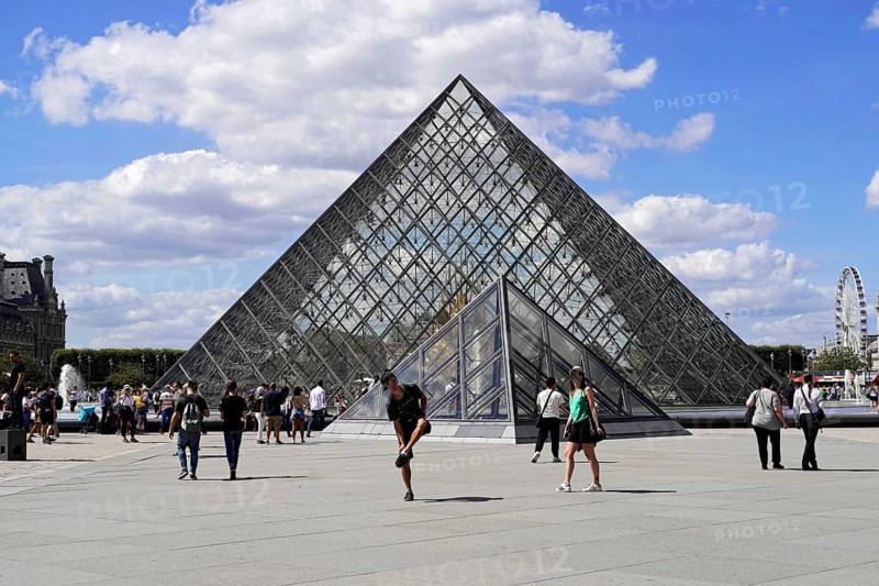 Glass pyramid in the courtyard of the Palais du Louvre, Paris, France, Europe, Tourists walk in front of the glass pyramid of the Louvre in Paris under a cloudy sky, Europe
