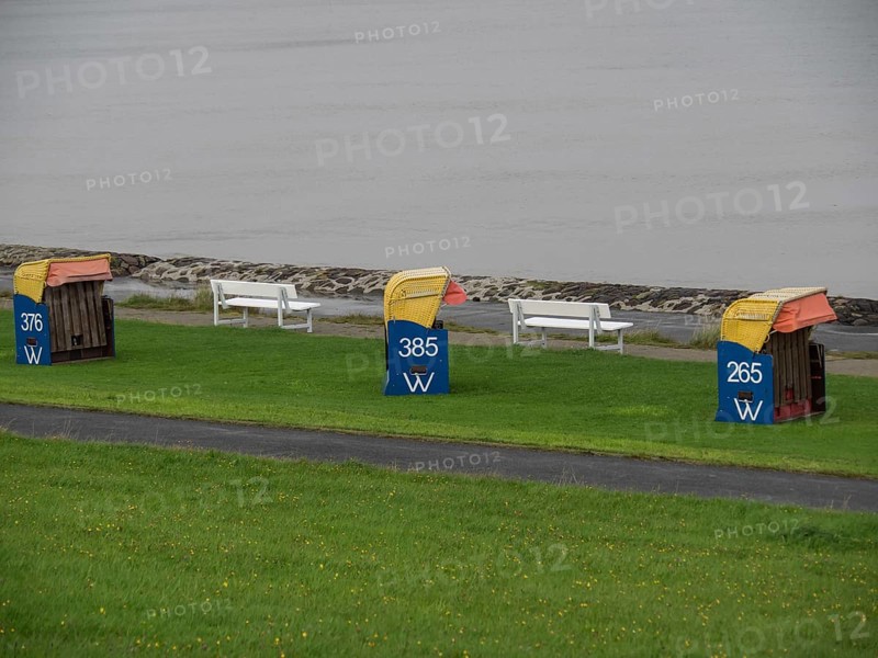 Three colourful beach chairs and white benches on a green lawn, quiet coastal atmosphere under a cloudy sky, cuxhaven, germany