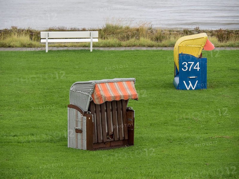 A single beach chair and a bench stand on a green meadow by the sea, cuxhaven, germany