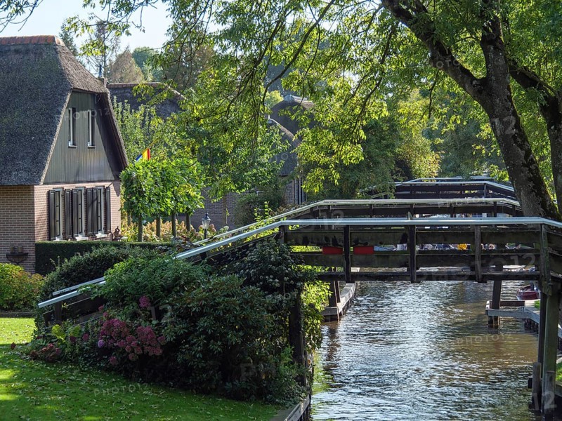 Wooden bridge over a canal, surrounded by trees and a house, with shadow effect through the leaves, giethoorn, the netherlands