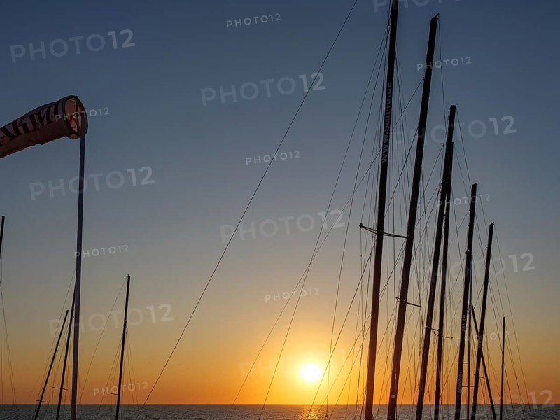 Sunset over the sea with silhouettes of sailboat masts in a peaceful atmosphere, De Haan, Flanders, Belgium, Europe