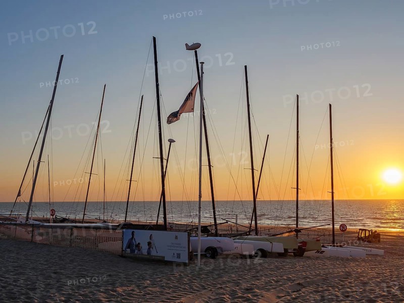 Boats with masts on the beach at sunset, calm atmosphere, warm light and sea in the background, De Haan, Flanders, Belgium, Europe