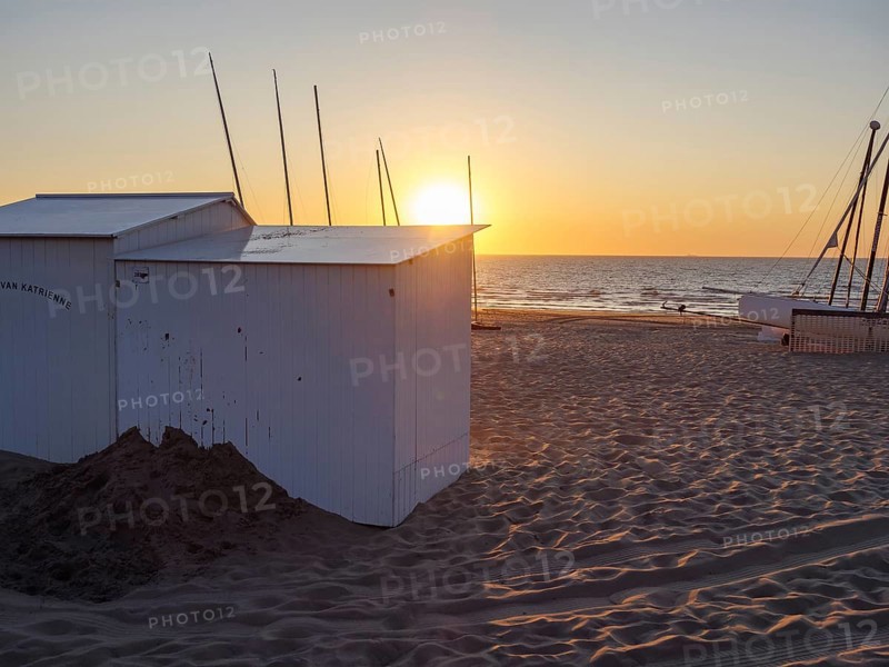 Sunset on the beach with white huts and a boat, warm colours and a calm atmosphere, sea in the background, De Haan, Flanders, Belgium, Europe