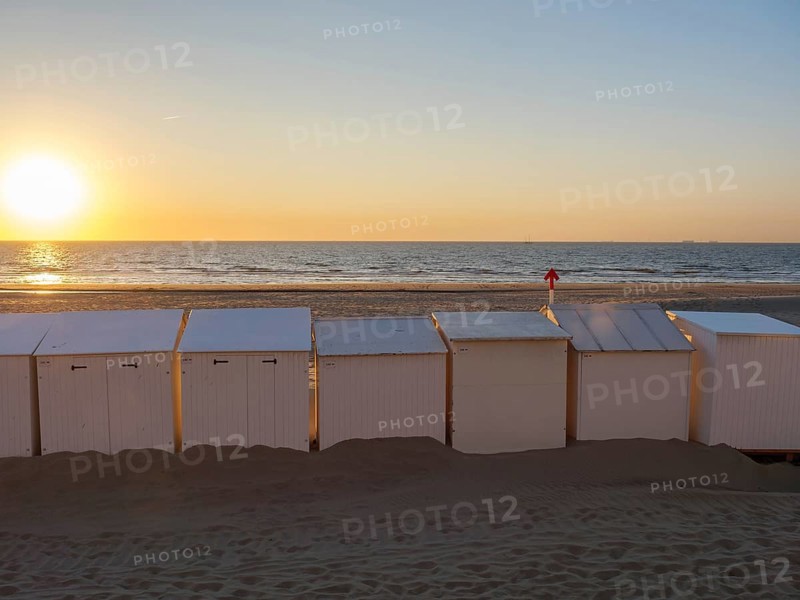 Beach with white huts, sunset over the sea, warm orange colours and calm atmosphere, De Haan, Flanders, Belgium, Europe