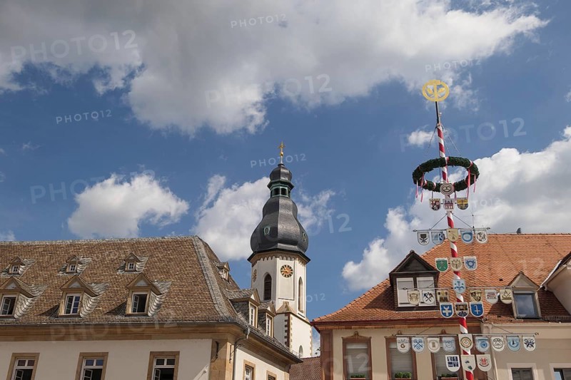 Historic buildings and a church tower decorated with coats of arms and a maypole under a cloudy sky, speyer, germany
