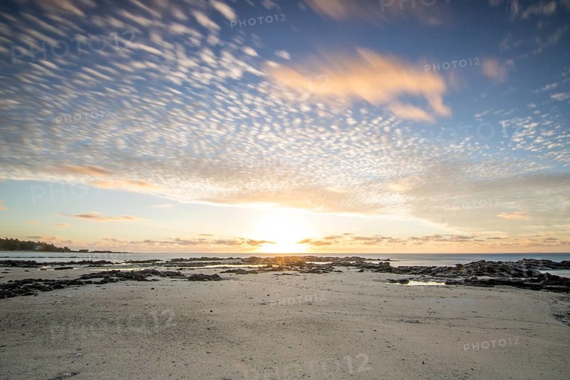 Sunrise over the sea with gentle waves. Sandy beach with lava rocks and blue water alternating with blue water. Island in the Indian Ocean, beach out of the blue, Trou d'Eau Douce, Mauritius, Africa