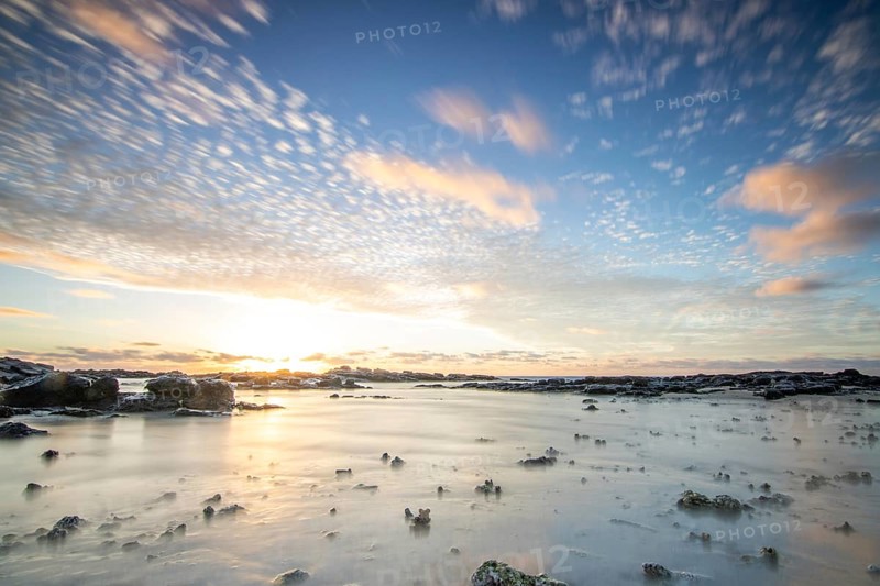 Sunrise over the sea with gentle waves. Sandy beach with lava rocks and blue water alternating with blue water. Island in the Indian Ocean, beach out of the blue, Trou d'Eau Douce, Mauritius, Africa