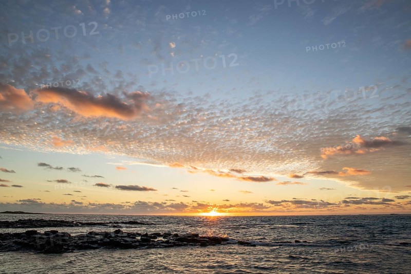 Sunrise over the sea with gentle waves. Sandy beach with lava rocks and blue water alternating with blue water. Island in the Indian Ocean, beach out of the blue, Trou d'Eau Douce, Mauritius, Africa