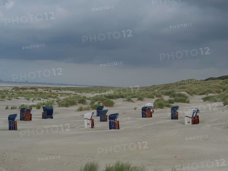 Scattered beach chairs on a sandy beach between grass and dunes under threatening clouds, Juist, North Sea, Germany, Europe