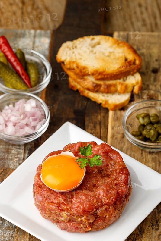 Steak tartare with open egg on wood