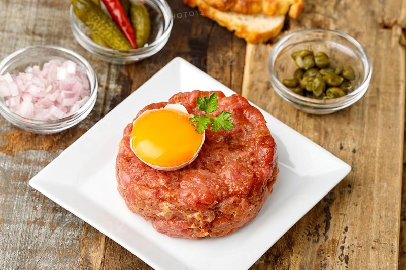 Steak tartare with open egg on wood