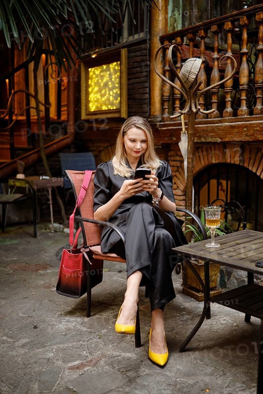 A stylish woman came to a wine bar, sat on the terrace and writes a message to her friends on her smartphone that she is waiting for them