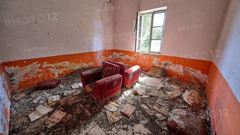Abandoned room with worn red armchairs and orange-coloured walls. The floor is covered with dirt and peeling plaster, signs of neglect, lost place, World War II bunker, barrack, Kalavarda, Rhodes, Dodecanese, Greek Islands, Greece, Europe