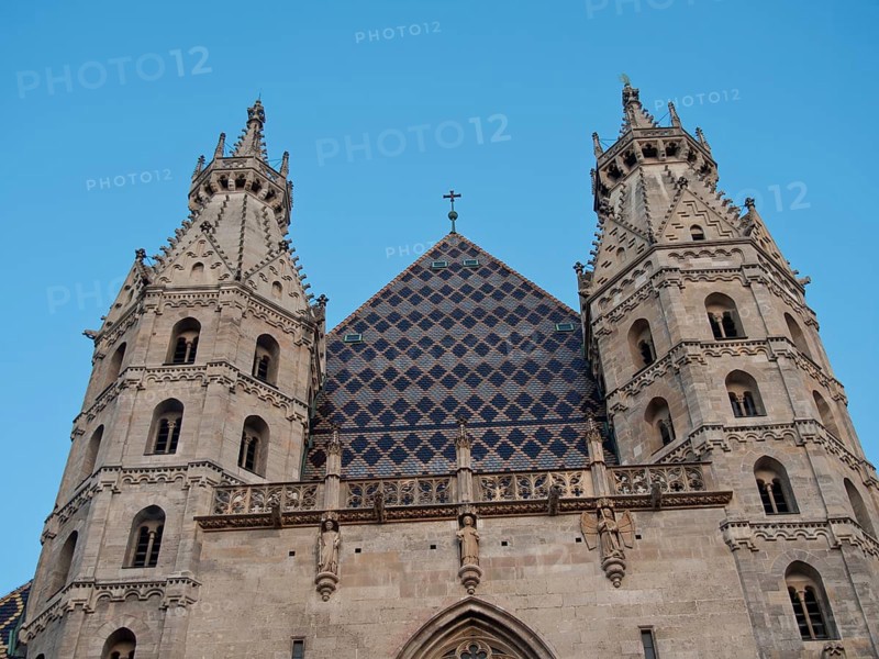 Front view of a Gothic cathedral with twin spires and a cross in the centre of the roof under a blue sky, Vienna, Austria, Europe
