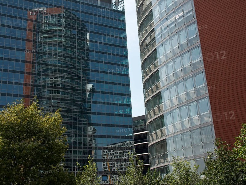 Two modern, glazed high-rise buildings with reflections and trees in the foreground, Vienna, Austria, Europe