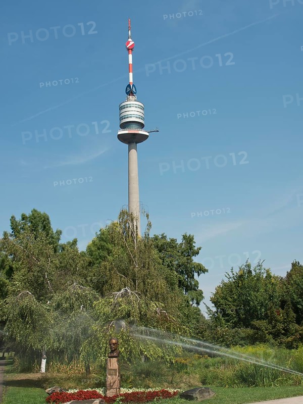 A tall television tower in a park with trees and a running irrigation system, Vienna, Austria, Europe