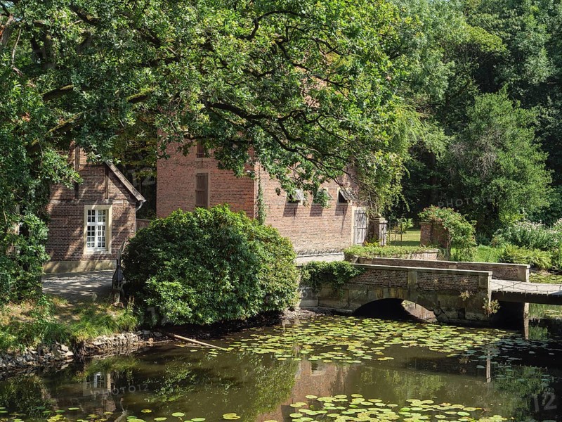 Rural idyll with a pond full of water lilies and a charming stone bridge flanked by old brick buildings, ochtrup, münsterland, germany