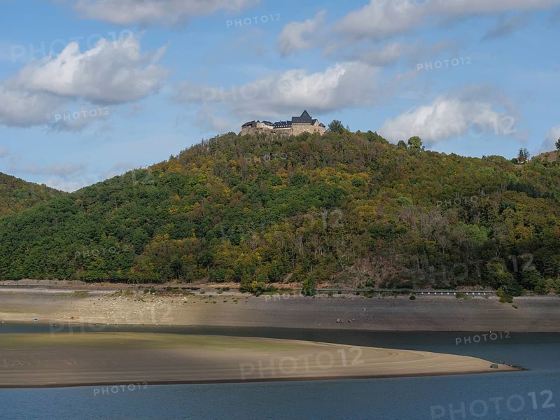 A striking castle overlooks the scene from a wooded hill sloping down to the banks of a river, under a bright sky with cloud formations, Waldeck, Hesse, Germany, Europe