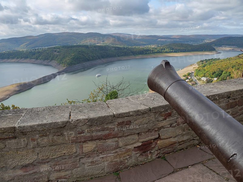 View from a stone wall with a cannon onto a lake surrounded by wooded hills under a cloudy sky, Waldeck, Hesse, Germany, Europe