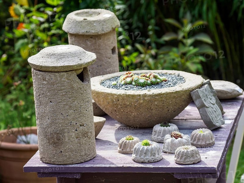 A garden area with rustic stone sculptures and small flowering decorations on a wooden table against a green background, SChermbeck North Rhine-Westphalia, Germany, Europe