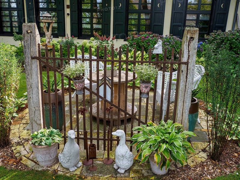 A rustic garden gate with statues and various plants surrounded by green landscape in front of a building, SChermbeck North Rhine-Westphalia, Germany, Europe