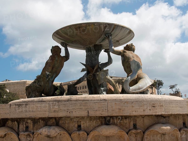 Bronze sculptures holding a large bowl of a fountain in a public square, valetta, mediterranean sea, malta