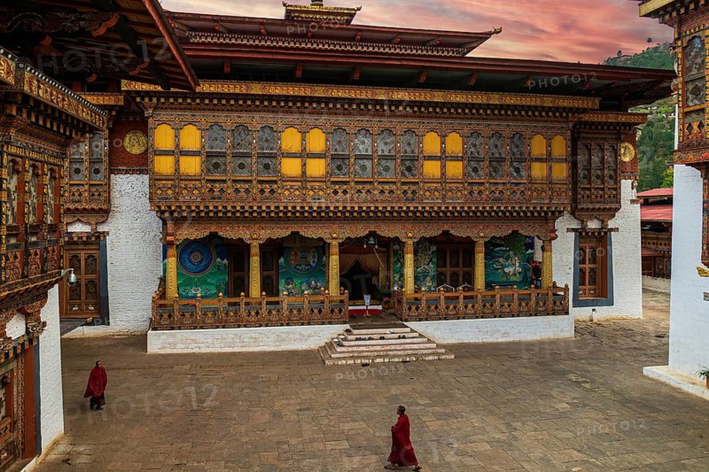 Two Buddhist monks in their traditional red dress walking in the monastery Punakha Dzong courtyard