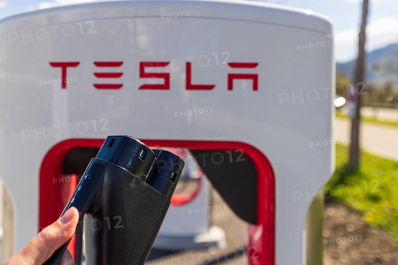 Tesla Superchargers on a parking lot, with a hand holding the CCS Type 2 plug