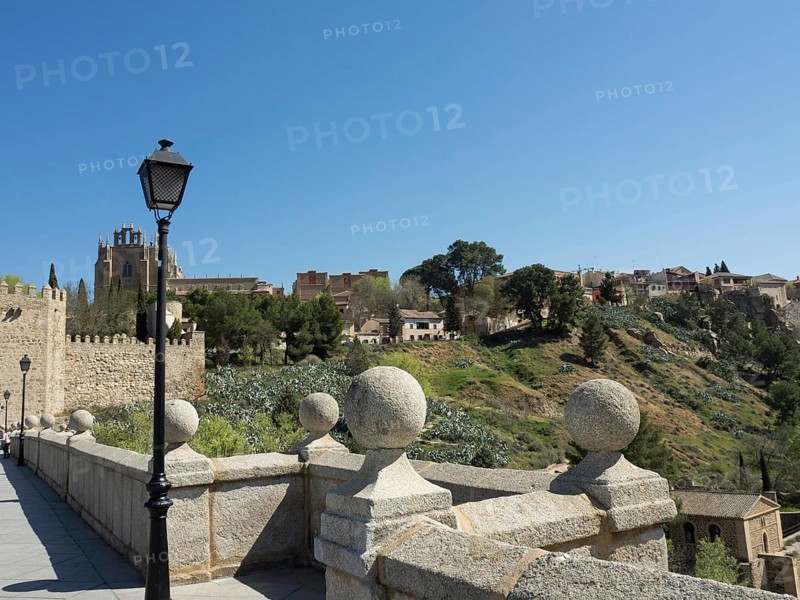 Picture of a bridge with a church in the background, surrounded by a green hilly landscape in bright sunlight, Toledo, Spain, Europe