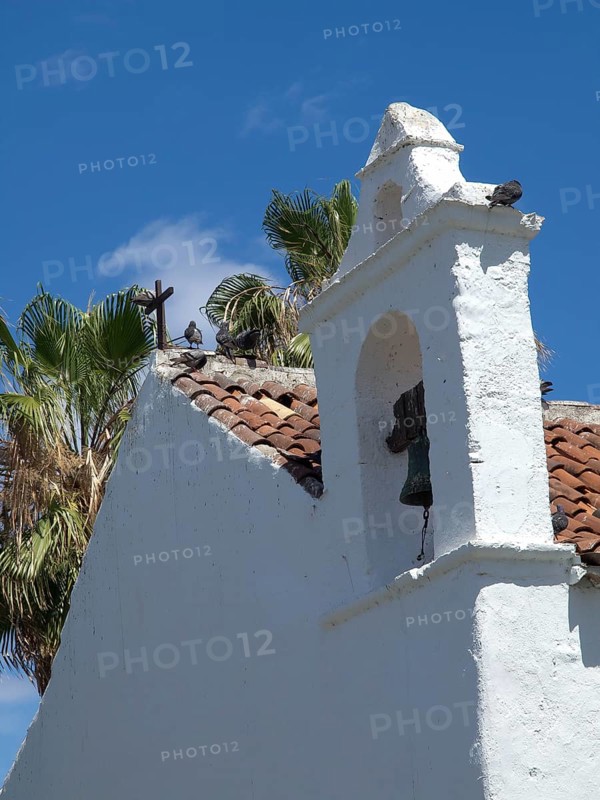White church with a bell tower and a cross on the roof, pigeons sitting on the roof