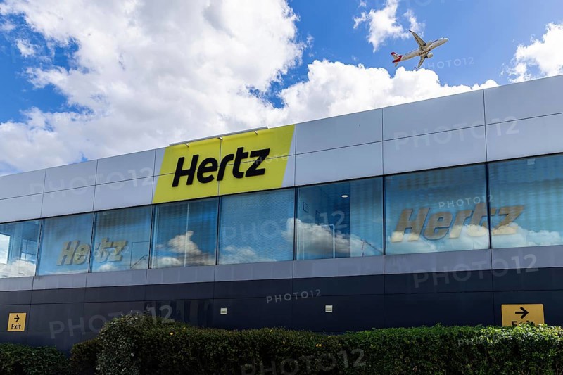 Hertz Car Rental at London Heathrow Airport with a plane flying over the building