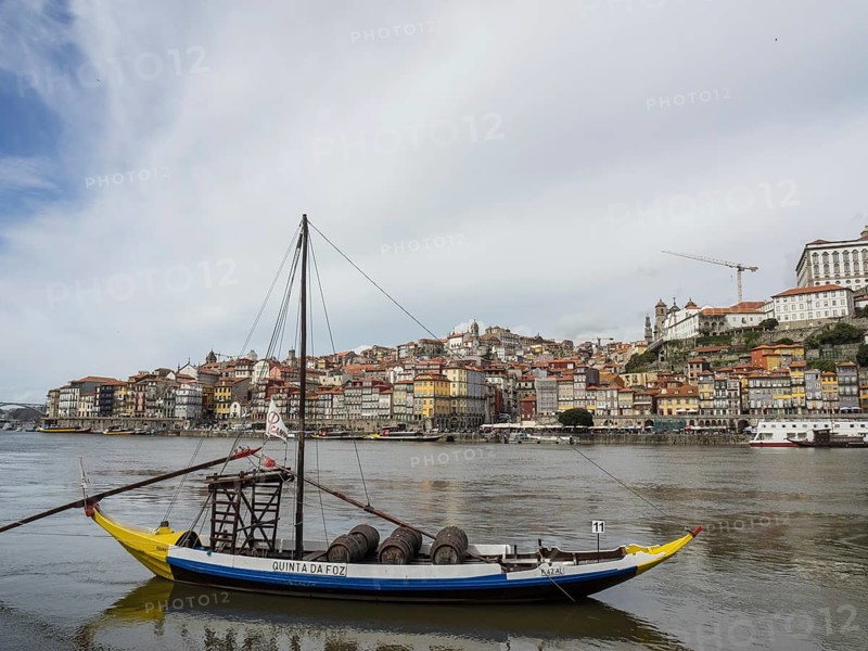 A boat with wine barrels floats on a river in front of a historic city, Porto, Douro, Portugal, Europe
