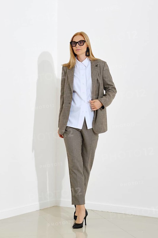 A full-length portrait of a professional woman in checkered suit walking confidently in a modern office
