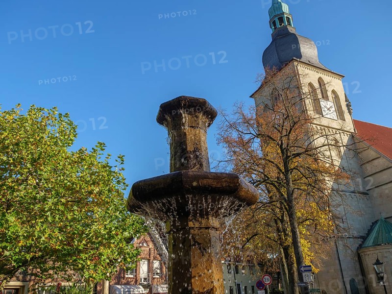 Water gushing through fountain and church tower with autumnal deciduous trees and blue sky, nottuln, münsterland, germany