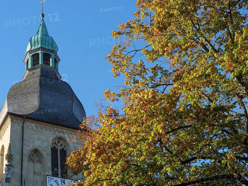 Church tower rises into a clear, sunny autumn sky, surrounded by colourful leaves, nottuln, münsterland, germany