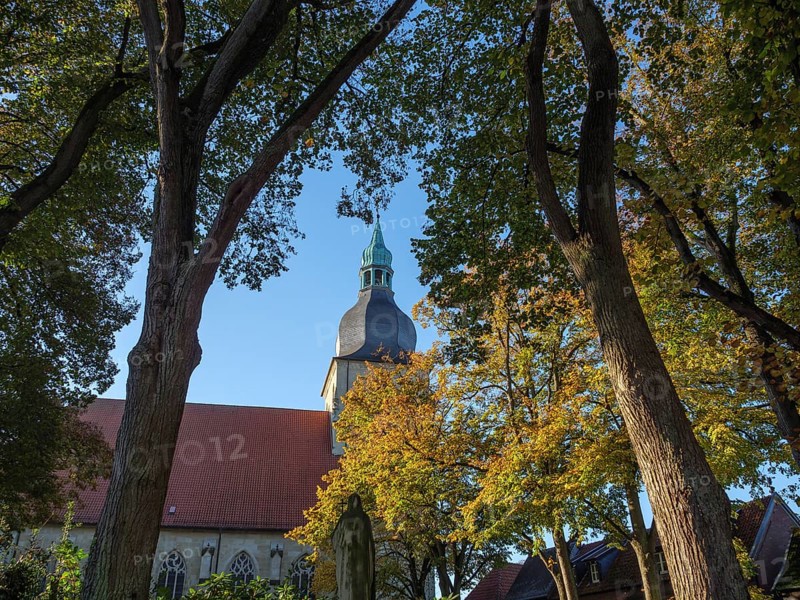 At the beginning of autumn, trees form a frame, in the centre a church with a green steeple under a blue sky, nottuln, münsterland, germany