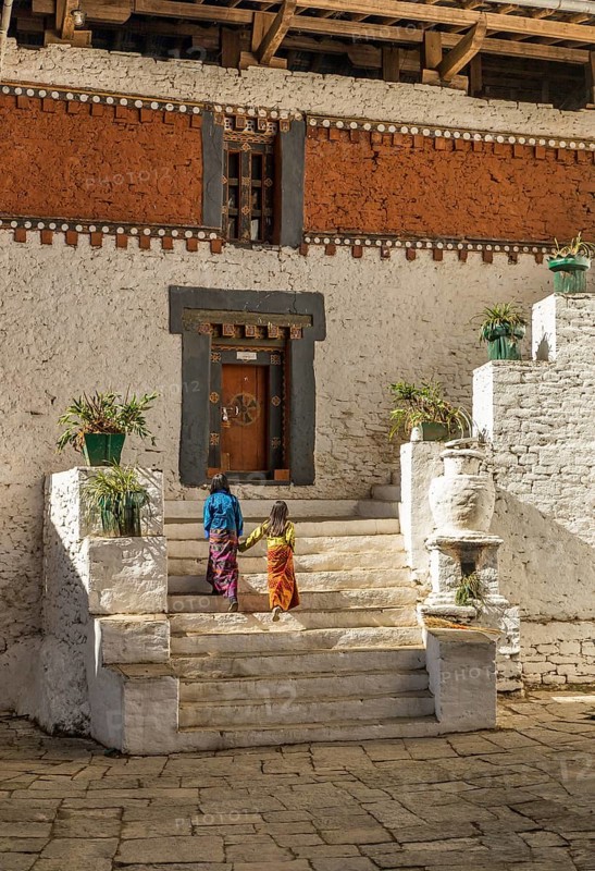 Two kids in colourful traditional clothes walking up the stairs inside Trongsa dzong